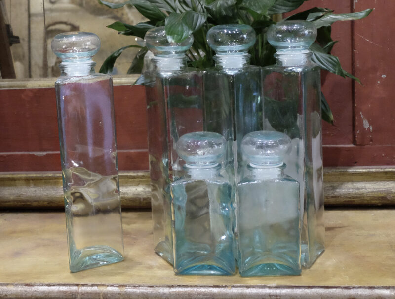 Set of triangle shaped big bottles in blown glass, with hermetic cap. Dimensions: 9x38 cm circa. Vintage furnishing accessories.